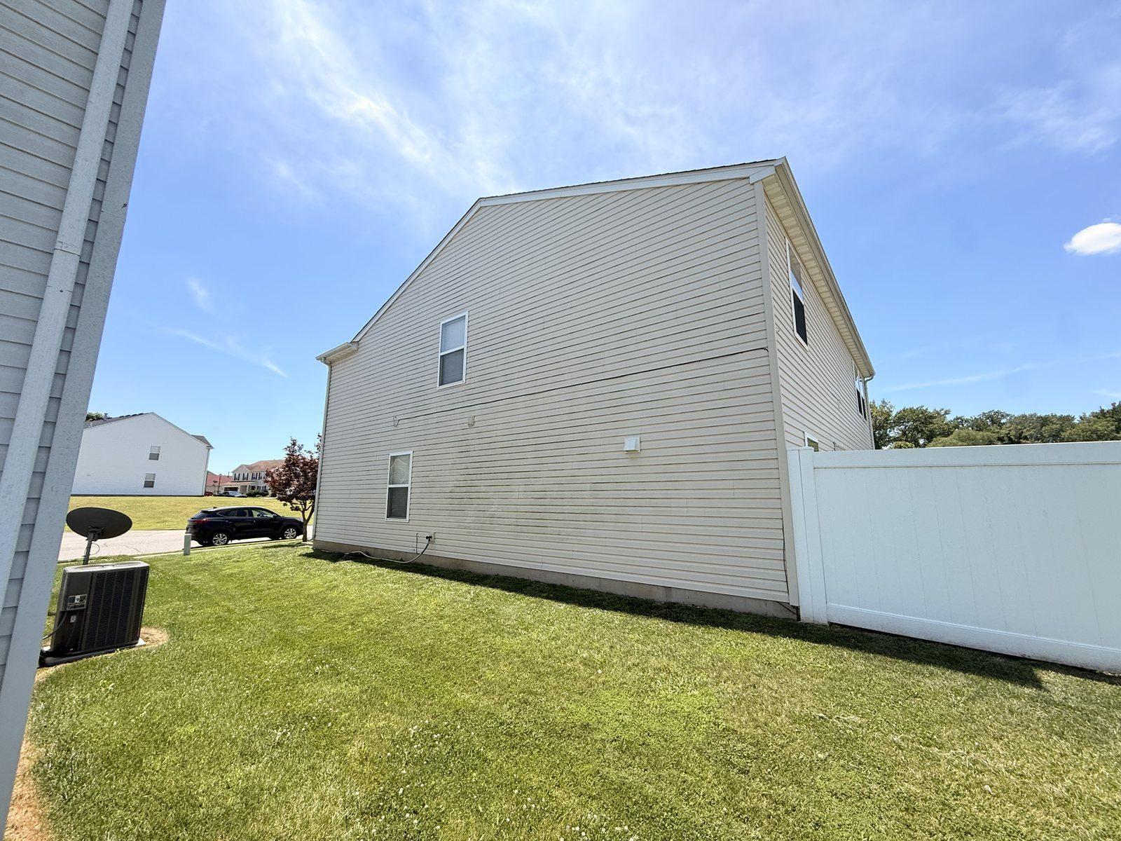 Before soft wash — algae on side-wall siding with windows and white fence